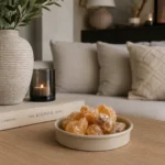 Beige metalen geurblokjeshouder met amberblokjes op een modern dressoir naast een vaas en woonaccessoires.