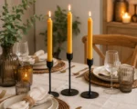 Okergele dinerkaarsen op een modern gedekte houten eettafel tijdens een sfeervol diner.
